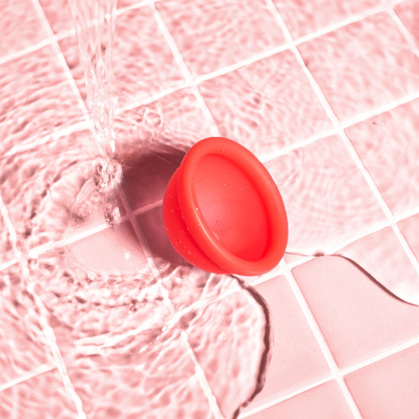 Disco menstrual vermelho sobre azulejos rosa com água